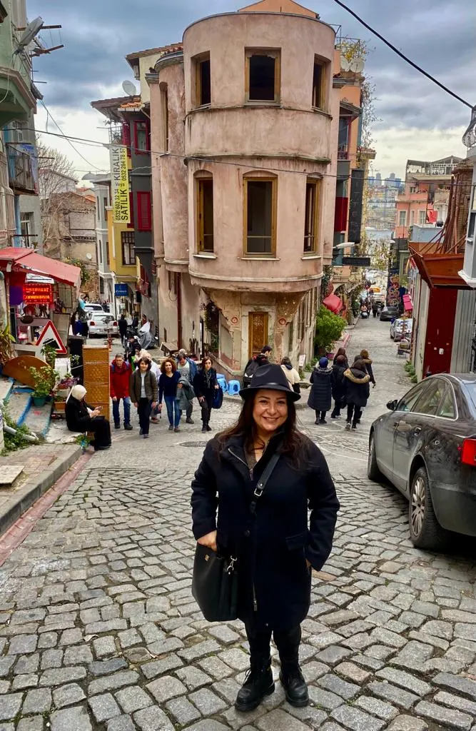 Ayşe Tokkuş Bayar, guide francophone, dans une rue pavée de Balat devant une maison historique à la façade arrondie
