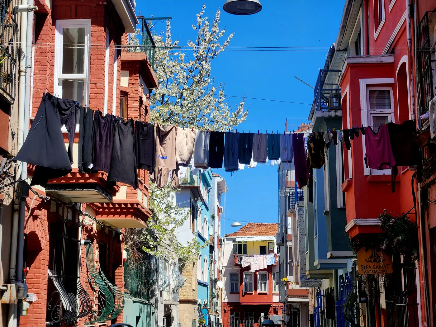 Du linge suspendu entre les maisons colorées d'une rue de Balat sous un ciel bleu vif