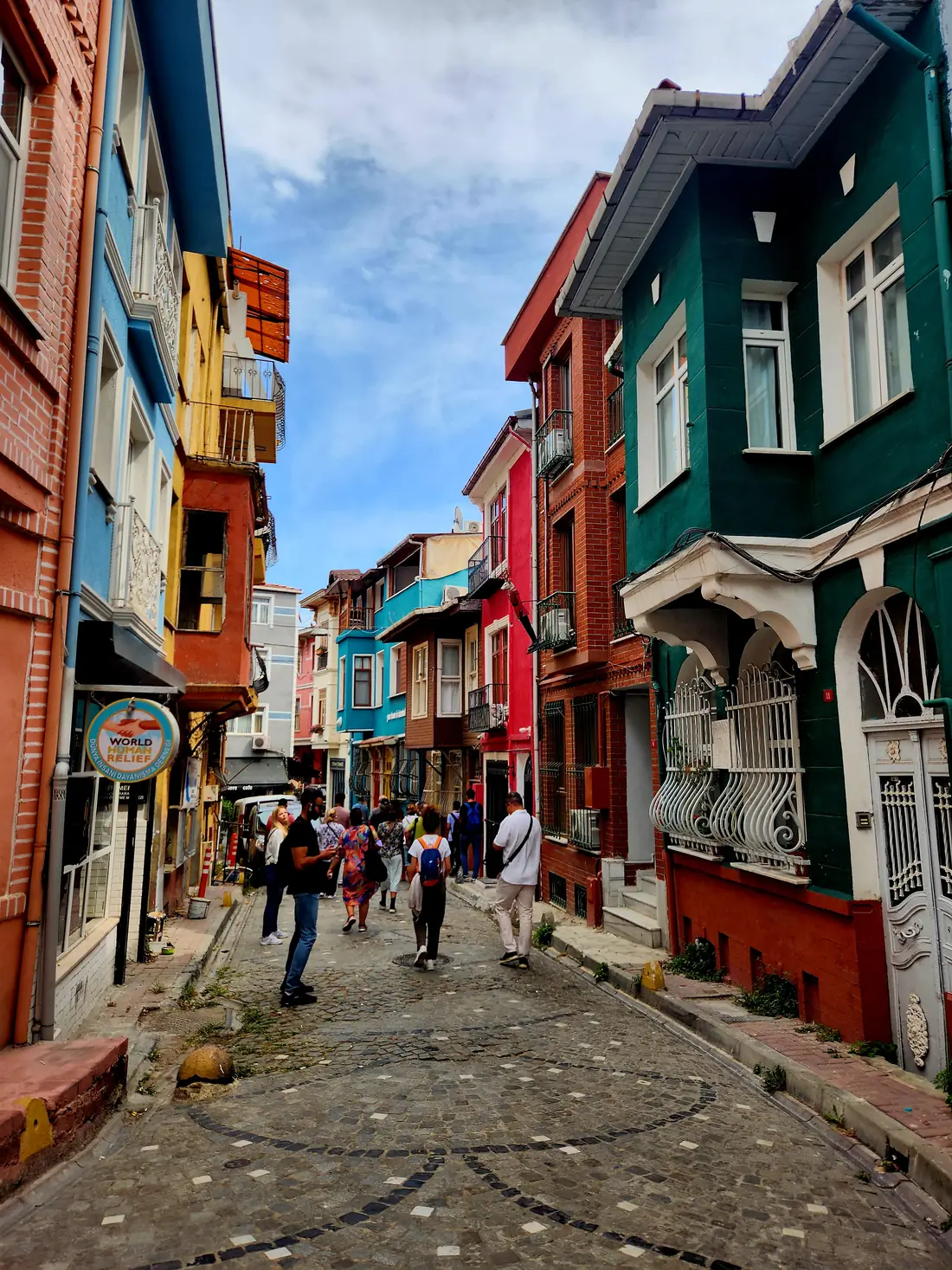 Ruelle pavée de Balat bordée de maisons colorées à encorbellement, avec des promeneurs sous un ciel d'été