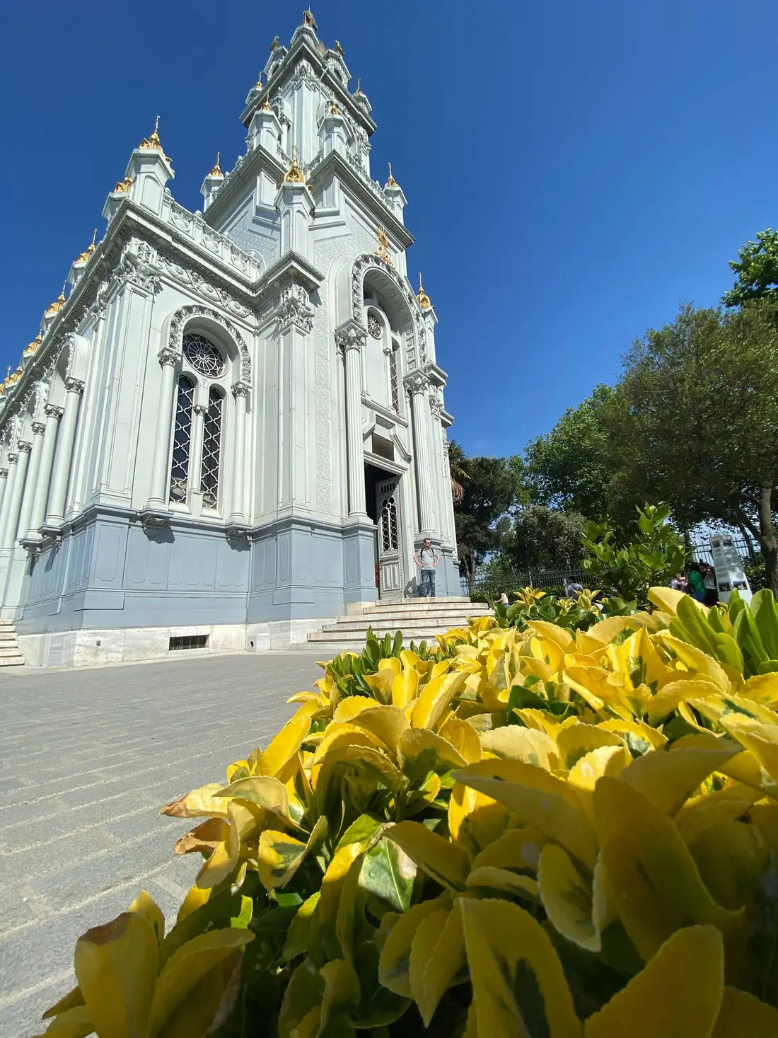 L'église de fer Sveti Stefan, façade claire aux clochetons dorés, derrière un parterre de feuillages jaunes